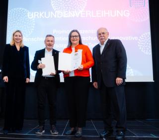 Zwei Frauen und zwei Männer auf einer Bühe, zwei halten eine Urkunde in den Händen